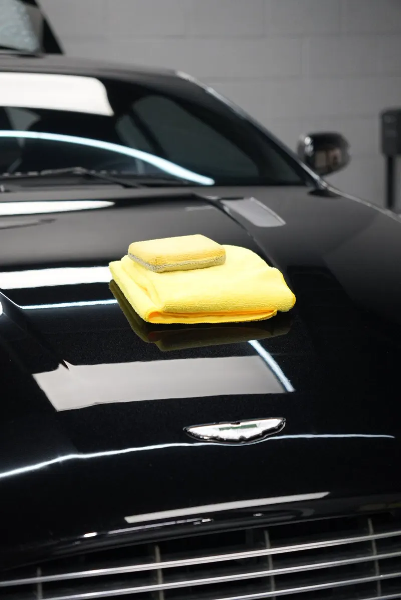 A folded microfiber towel and a foam applicator block resting on the glossy black hood of a vehicle.