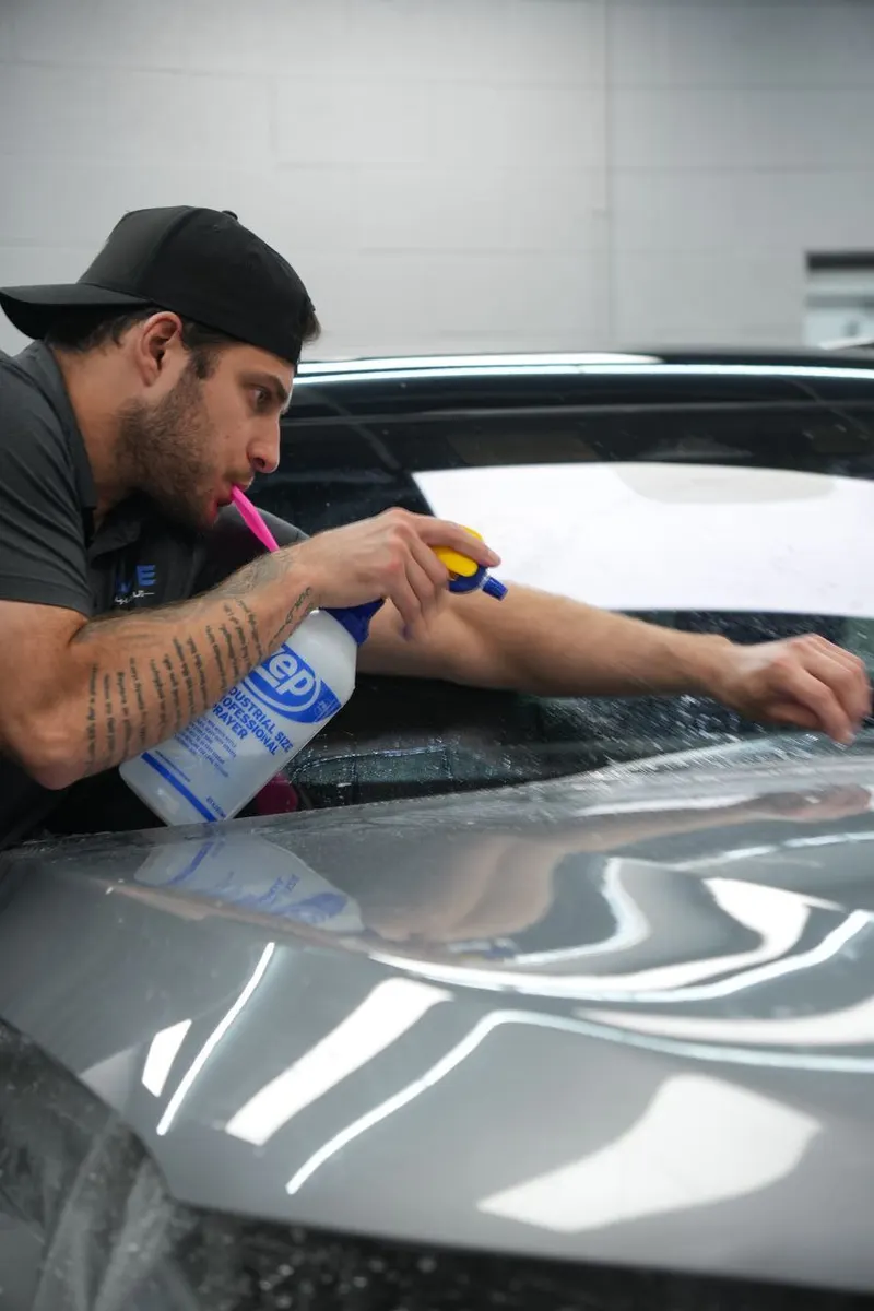 A technician applies solution to a vehicle panel edge with a small brush during film installation.