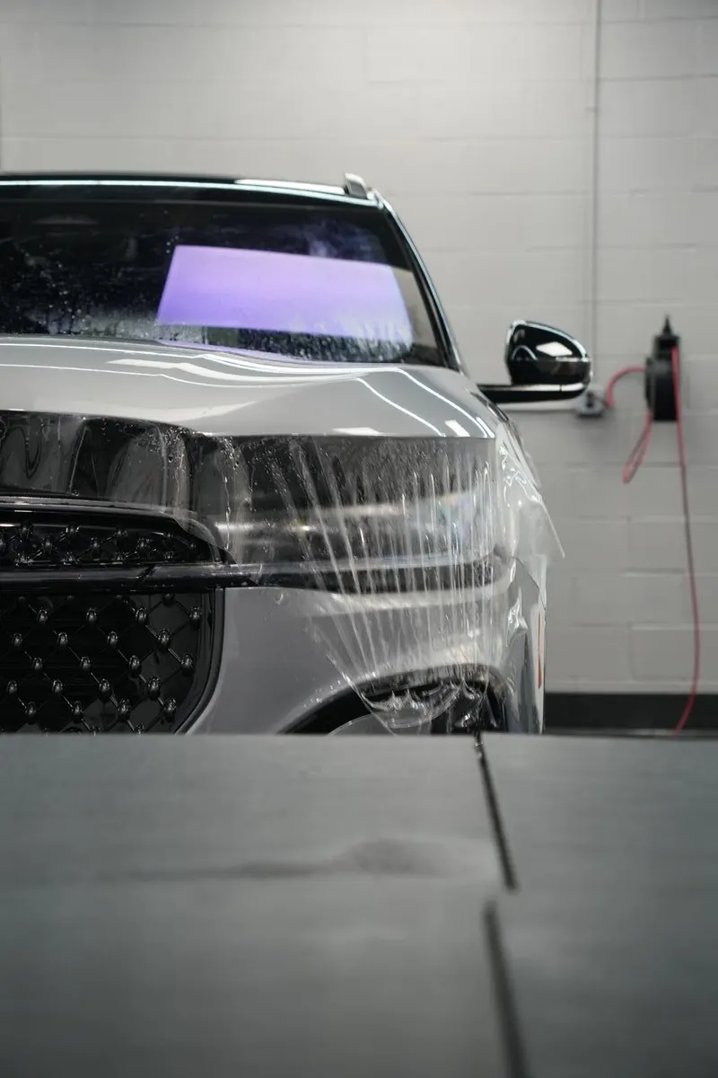 Front bumper and fender of a vehicle wrapped in clear film, with water beaded on the surface.