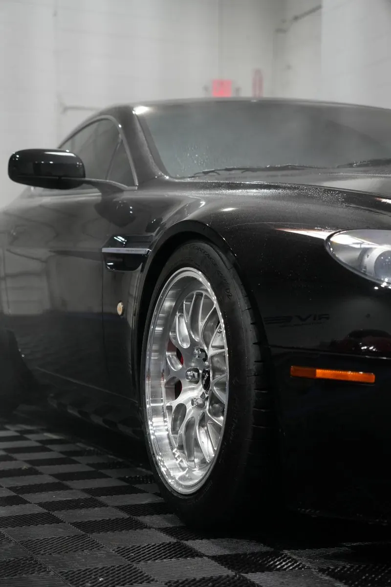 Close-up of a vehicle's wheel, tire, and front fender in a shop bay.